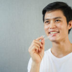 man smiling with hand holding dental aligner retainer