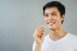 man smiling with hand holding dental aligner retainer