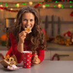 Happy young woman having eating christmas cookies in kitchen