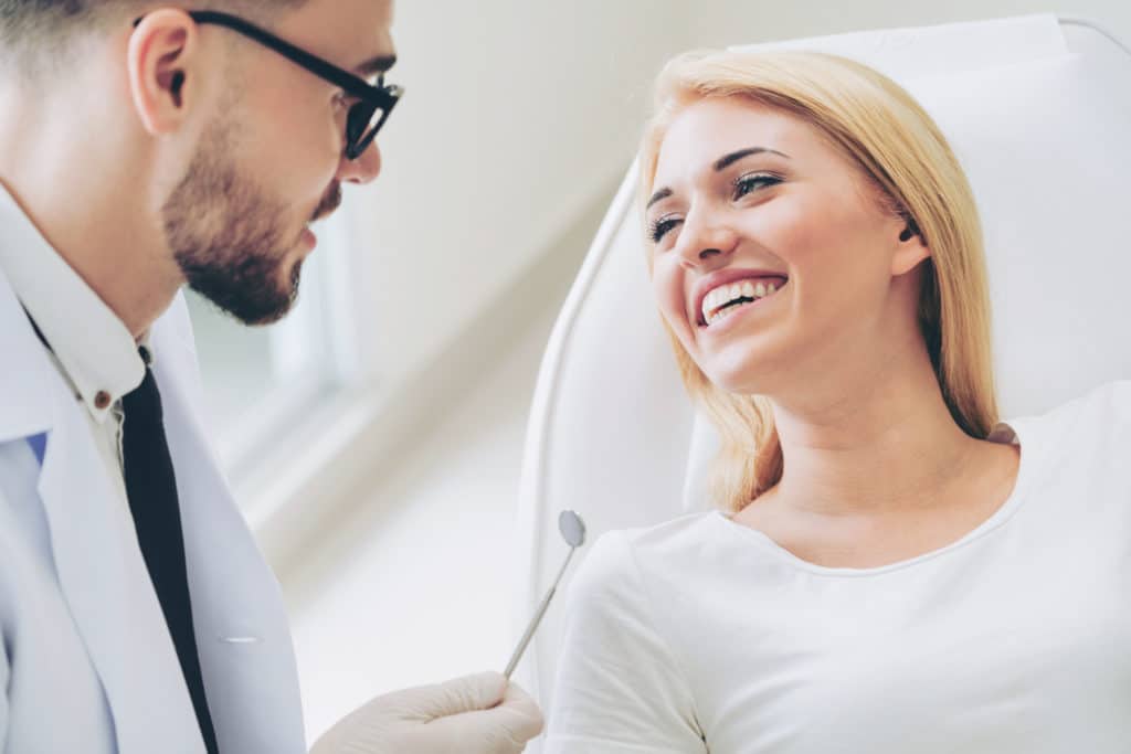 Young dentist talks with patient in dental clinic.