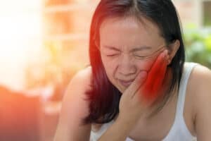 Woman grasping her mouth in pain from TMJ and TMD symptoms.