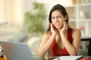 Stressed student holding jaw in discomfort at home, showing signs of TMJ disorder and temporomandibular joint pain caused by tension or teeth grinding