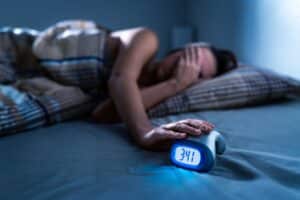 Woman lying awake in bed next to alarm clock, illustrating sleep disturbances related to insomnia, sleep apnea, TMJ disorder, or nighttime anxiety